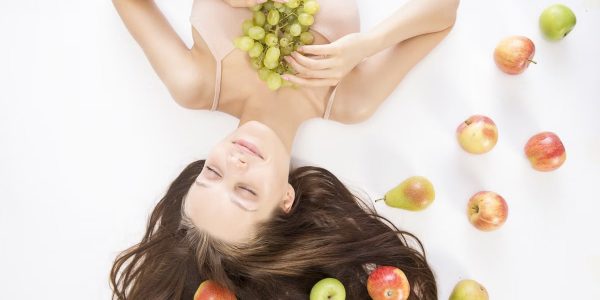 Woman lying down with fresh fruits symbolizes beauty and wellness.