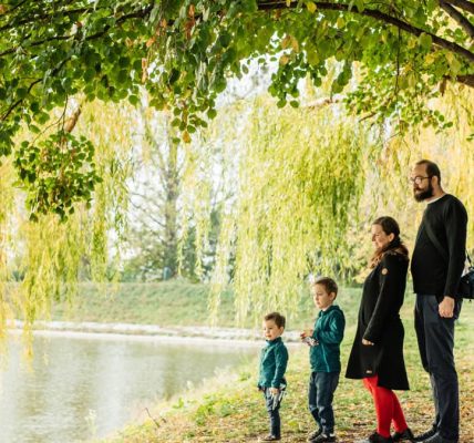 A family enjoys a peaceful walk by a lakeside under a willow tree during autumn.