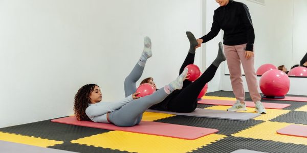 Women engaged in pilates class using pink balls and yoga mats indoors at a gym.